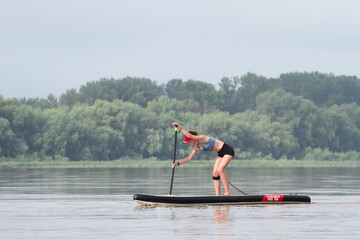 Sporty girl surfing on stand up paddle (SUP) at calm summer morning on the Danube river