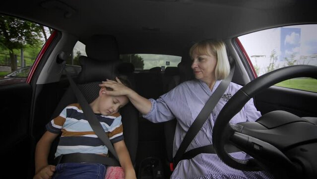 Grandmother and grandson are driving in the car. The boy fell asleep on the seat