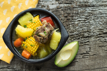 Sancocho, typical Colombian food in a black bowl on a rustic wooden background.