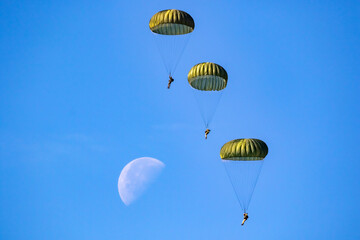 Military parachutist paratroopers parachute jumping out of a air force planes on a clear blue sky day with the moon.