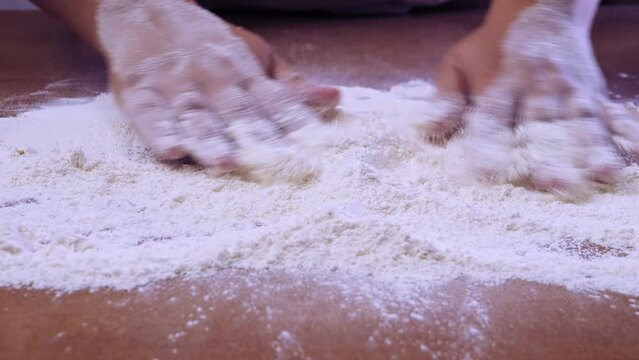 Women's hands scatter white flour for baking on a wooden table. Medium plan