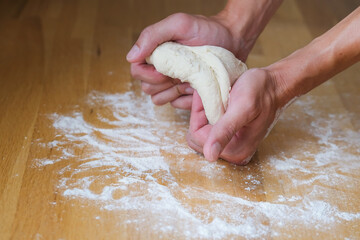 Person crumples and stretches a lump of dough in his hands in front of a table with white flour