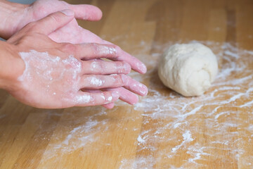 Hands in flour against a lump of dough while making pizza and baking