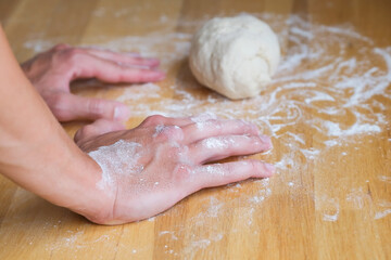 Hands of a baker leaning on a table in front of a lump of dough