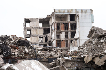 A ruined building against a gray sky with piles of concrete rubble and construction debris in the...