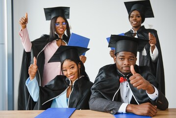education, graduation and people concept - group of happy international graduate students in mortar boards and bachelor gowns with diplomas