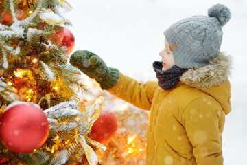 Little boy admiring artificial Christmas tree decorated with gold and red balls and flowers....
