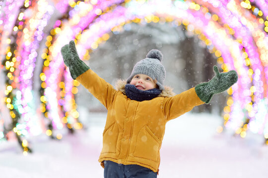 Little boy is admiring a large glowing street decoration on Christmas fair. Traditional city Xmas market in the open air. Modern urban festive decoration.