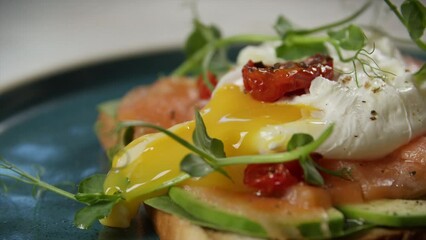 Close-up A poached egg is cut on a sandwich with salmon and avocado.