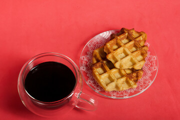 Fluffy waffles. They lie on a saucer. Next to a cup of coffee. The background is pink. Shot close-up.