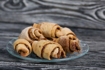 Croissants with cinnamon. Rolls with cinnamon. They lie on a saucer. Background from black pine boards. Shot close-up.