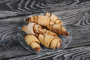 Croissants with cinnamon. Rolls with cinnamon. They lie on a saucer. Background from black pine boards. Shot close-up.