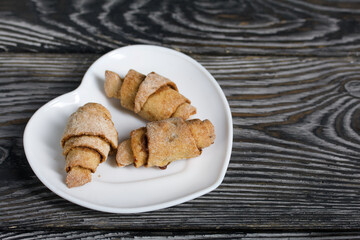 Croissants with cinnamon. Rolls with cinnamon. They lie on a saucer. Background from black pine boards. Shot close-up.