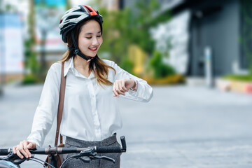 Young Asian businesswoman wearing helmet and standing on a city street with bicycle looking at sky...
