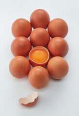 Brown whole eggs, cracked brown egg with a yolk and eggshell. Row of brown eggs and single broken egg with a yolk on a white background. Shallow depth of field. 
