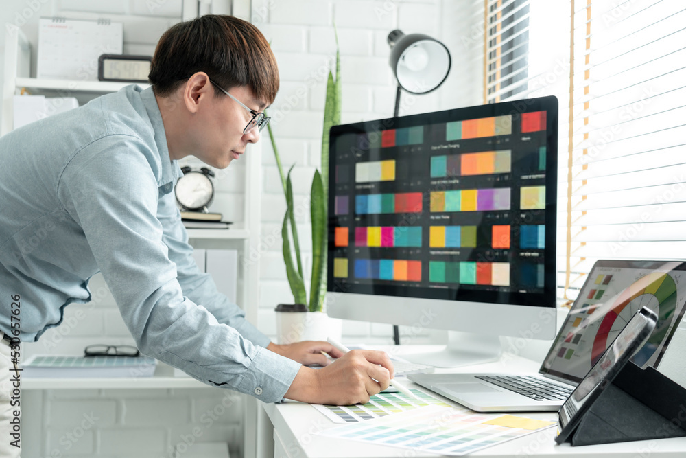 Poster male graphic designer is standing to choosing color swatch samples on multiple screens and working g
