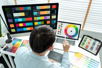 Male graphic designer is choosing color swatch samples on multiple screens and sketching on tablet