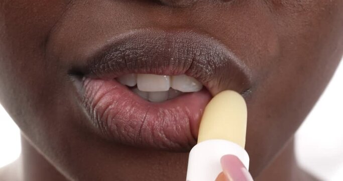 Close up view of a black woman moisturizing her lips by applying lip balm to her lips. Isolated on a white background.