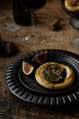 Puff pastry with figs, brie cheese and thyme. Appetizer for wine. Starters in a black ceramic plates on a vintage wooden table