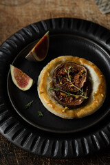 Puff pastry with figs, brie cheese and thyme. Appetizer for wine. Starters in a black ceramic plates on a vintage wooden table. Close up