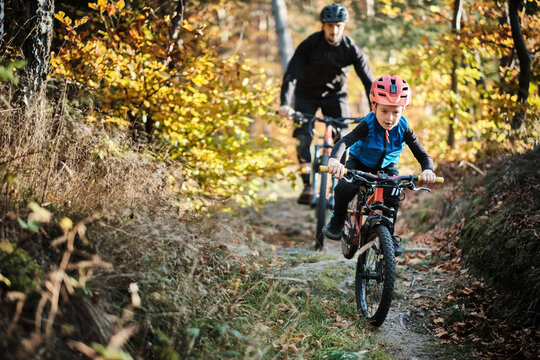 Father and son mountain biking on path in woods