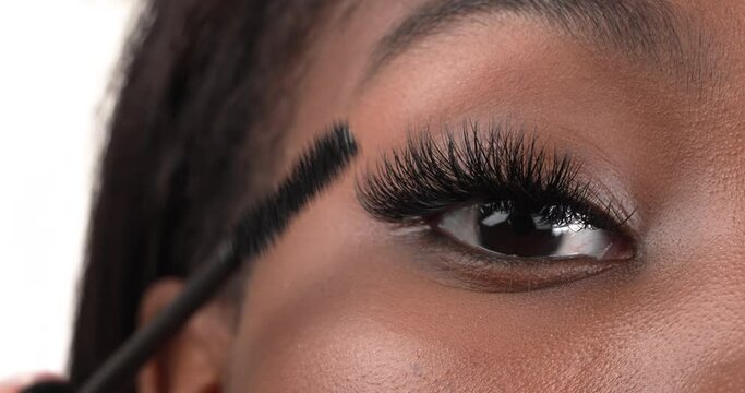 Close up view of a black woman eye. Applying mascara using a brush to her eyelashes. Isolated on a white background.