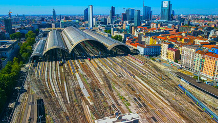 Aerial view of the station where trains arrive. An old arched structure made of metal and glass above the station poles. Tourism. Transport. Skyline with tall buildings. Italy, Milan, 09.2022