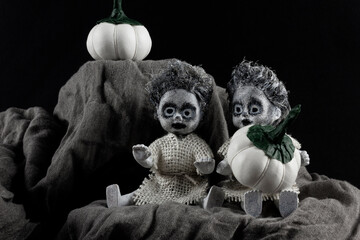 Happy halloween holiday. Two scary zombie dolls with white pumpkins on a dark background.