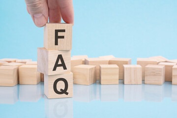 man puts wooden blocks with the word FAQ. collection of frequently asked questions on any topic and...