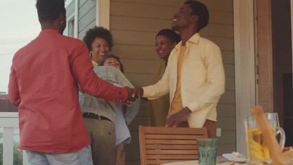 Medium shot of two cheerful African American couples with two kid boys meeting on front porch of house, hugging and greeting each other with joy, getting together to have dinner