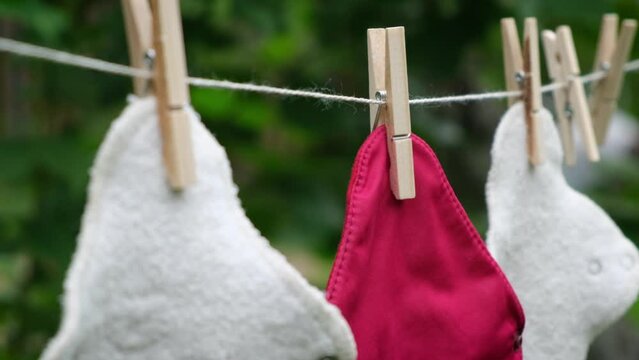 Close up focus crossing three reusable cloth sanitary menstrual pads hanging to dry on clothesline in the garden. Zero waste period. Feminine washable, eco friendly personal hygiene supplies.