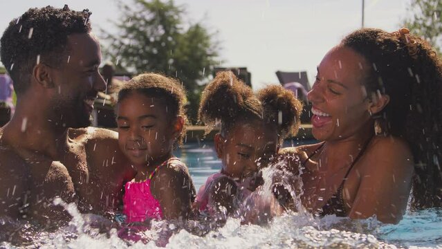 Family on summer holiday with two girls being held in swimming pool by parents splashing - shot in slow motion