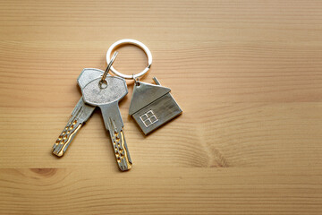 Keys with a keychain in the form of a house lie on a wooden table. Buying a house, apartment. The concept of real estate transactions.