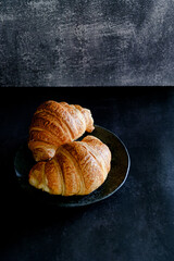 Delicious breakfast with fresh and baked french croissants on a dark concrete background. Space for text