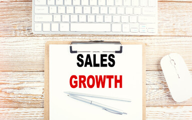 SALES GROWTH text on a clipboard with keyboard on wooden background