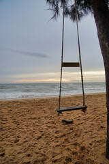 Vertical picture of a swing chair tied to a tree with a backdrop of the evening sea and the setting sun.