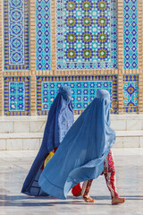 Women wearing blue burka in front of blue mosque