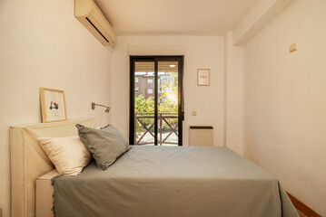 bedroom with double bed with headboard with gray cushions brown aluminum balcony overlooking a garden