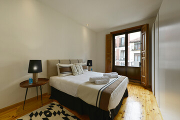 bedroom with double bed with fabric headboard, matching cushions, matching bedspread, wooden floor and balcony with views and wooden shutters