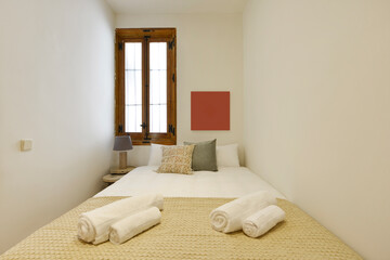 Fototapeta na wymiar narrow bedroom with double bed, matching cushions, matching bedspread and wooden window