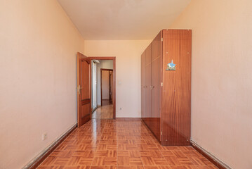 Empty bedroom with glossy wooden three-door wardrobe, stoneware floor and matching front door