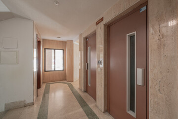 Landing of an apartment building with brown painted metal elevator doors and brown aluminum windows © Toyakisfoto.photos
