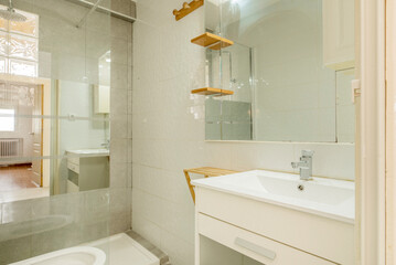 Small bathroom with white wooden cabinet with square mirror, mirror screen in the shower and wooden shelves
