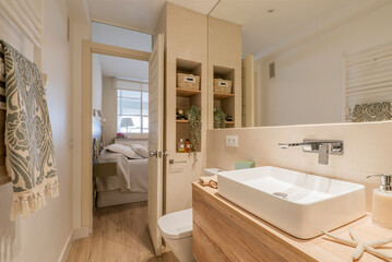 Fototapeta na wymiar Bathroom with wooden vanity with frameless mirror, alcove with shelves and white porcelain sink