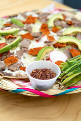 top view of Mexican food Tlayuda de cecina y chorizo and its preparation ingredients on a wooden table, frijoles, beans, cecina, sausage, lettuce, sauce, fruit water