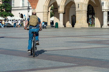 A cyclist with a tourist backpack on his back rides a bicycle on a sunny day in the city square, healthy lifestyle, sustainable transport in European cities, market square in Krakow