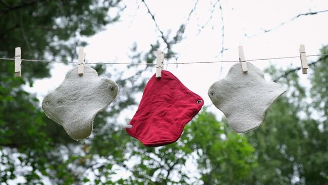 Woman removes dried reusable cloth sanitary menstrual pads from a clothesline in the garden. Zero waste period. Feminine washable, eco friendly personal hygiene supplies. Womens health care. 