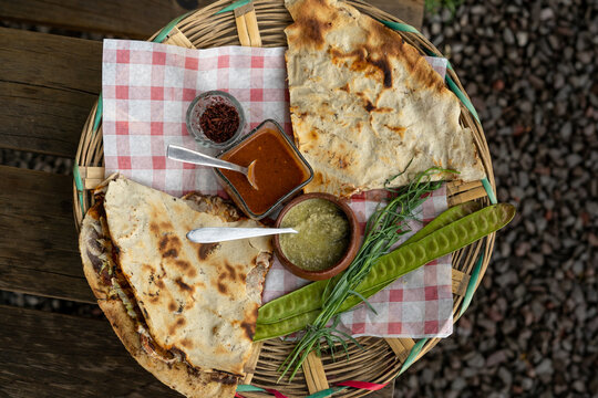 top view of Mexican food Tlayuda de cecina y chorizo and its preparation ingredients on a wooden table, frijoles, beans, cecina, sausage, lettuce, sauce, fruit water