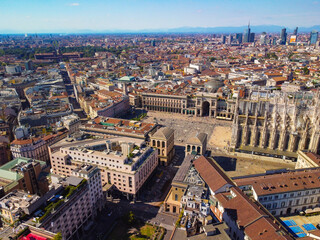 Fototapeta na wymiar Aerial view of Piazza Duomo in front of the Gothic cathedral in the center. Drone view of the gallery and rooftops during the day. Flight over the city. People in the city. Milan. Italy 2022