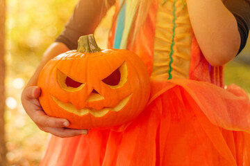 Carved festive pumpkin in the hands of a child dressed up for a celebratory party on Halloween day